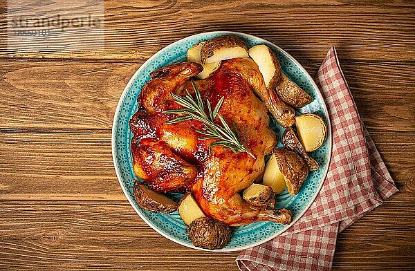 Leckeres gebratenes ganzes Huhn mit glasierter goldener knuspriger Haut auf großem Keramikteller Draufsicht auf hölzernem rustikalem Hintergrund Draufsicht  traditionelles leckeres Abendessen
