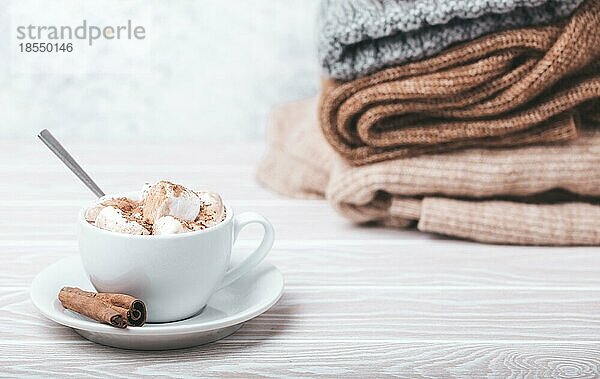 Cozy Winter Zusammensetzung  Tasse mit heißer Schokolade oder Kakao mit Marshmallow und Stapel von warmen gestrickte Kleidung auf weißem Holz rustikalen Hintergrund. Gemütliche und weiche Winter zu Hause  freier Raum für Text