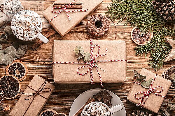 Weihnachtsgeschenk auf dem Holztisch mit eingewickelt Geschenkboxen Tannenbaum Zweig  Marshmallow Kakao Tassen dekoriert. Wrapping Weihnachtsgeschenk Draufsicht  gemütlich und tröstlich festliche Zusammensetzung flach legen