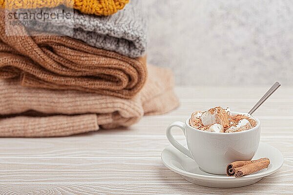 Cozy Winter Zusammensetzung  Tasse mit heißer Schokolade oder Kakao mit Marshmallow und Stapel von warmen gestrickte Kleidung auf weißem Holz rustikalen Hintergrund. Gemütliche und weiche Winter zu Hause  freier Raum für Text