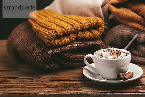 Cozy Winter Zusammensetzung  Tasse mit heißer Schokolade oder Kakao mit Marshmallow und Stapel von warmen gestrickte Kleidung auf Holz rustikalen Hintergrund. Gemütliche und weiche Winter zu Hause  freier Raum für Text