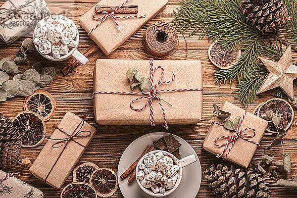 Weihnachtsgeschenk auf dem Holztisch mit eingewickelt Geschenkboxen Tannenbaum Zweig  Marshmallow Kakao Tassen dekoriert. Wrapping Weihnachtsgeschenk Draufsicht  gemütlich und tröstlich festliche Zusammensetzung flach legen