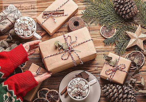 Weihnachten flach legen mit weiblichen Händen binden ein Band auf ein Geschenk  Geschenkboxen Tannenbaum Zweig auf hölzernen Hintergrund. Wrapping Xmas Geschenk Draufsicht  gemütliche festliche Zusammensetzung