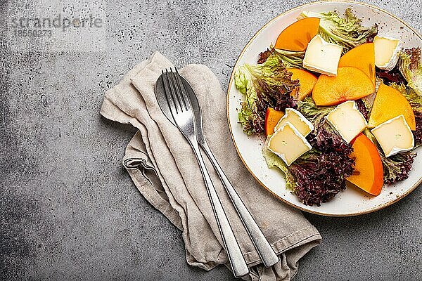 Draufsicht flach legen Kaki-Salat mit Brie-Käse  frischer Salat Blätter auf weißem Teller Stein grauem Hintergrund  Obstsalat der Saison als Vorspeise  vegetarische gesunde Lebensmittel Raum für Text