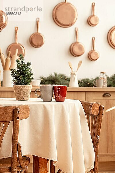 Zwei Teetassen auf einem Weihnachtstisch mit einem kleinen Baum in einer hellen  modern dekorierten Küche mit vielen Kupferpfannen an der Wand  Küchengeräten und -utensilien  Kerzen  Platz für Text