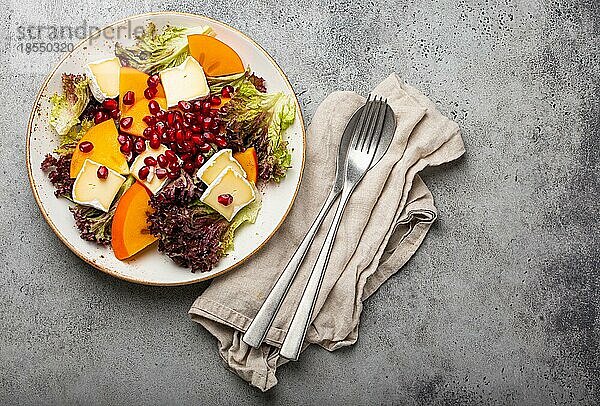 Draufsicht flach legen Kaki-Salat mit Brie-Käse  frischer Salat Blätter  Granatapfelkerne auf weißem Teller steingrauem Hintergrund  Obstsalat der Saison als Vorspeise  vegetarische gesunde Lebensmittel Kopie Raum