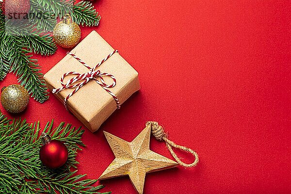 Weihnachten und Neujahr flach legen Zusammensetzung mit grünen Tannenzweig und Weihnachtsschmuck auf leuchtend roten Hintergrund  hölzerne Stern und in Bastelpapier eingewickelt vorhanden Draufsicht  Platz für Text