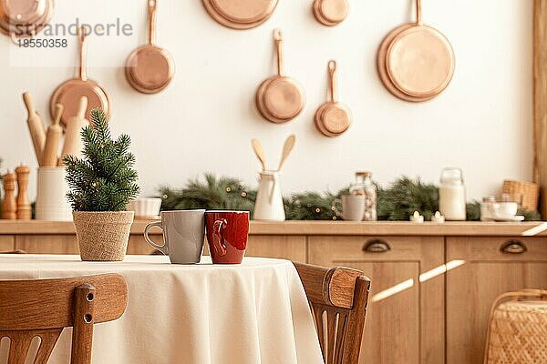 Zwei Teetassen auf einem Weihnachtstisch mit einem kleinen Baum in einer hellen  modern dekorierten Küche mit vielen Kupferpfannen an der Wand  Küchengeräten und -utensilien  Kerzen  Platz für Text