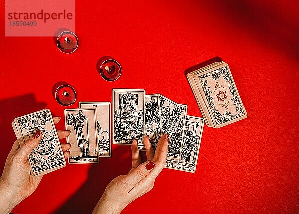 Esoterische Magie Zusammensetzung Draufsicht mit weiblichen Händen der Wahrsagerin Lesen Tarot-Karten auf rotem Hintergrund mit brennenden Kerzen  Magie  Okkultismus und Prognose Konzept