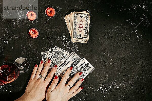 Esoteric Zusammensetzung Draufsicht mit weiblichen Händen der Wahrsagerin mit Glas Rotwein lesen Tarot-Karten auf schwarzem magischen Hintergrund Tisch  rot brennenden Kerzen  okkulte und Prognose  Kopie Raum
