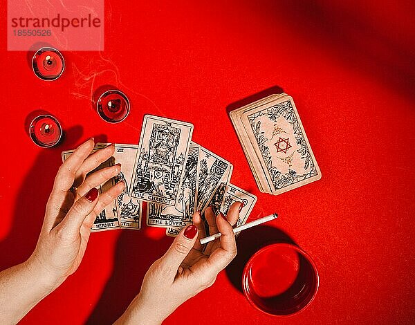 Esoterische Magie Zusammensetzung Draufsicht mit weiblichen Händen der Wahrsagerin mit Zigarette lesen Tarot-Karten auf rotem Hintergrund mit brennenden Kerzen  Magie  Okkultismus und Prognose Konzept