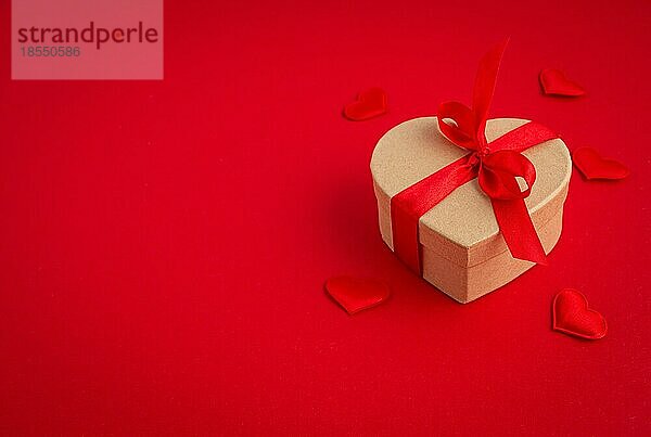Schöne minimale verpackt Geschenk-Box herzförmig mit roter Schleife Band auf rotem Hintergrund und kleine gepolsterte Herzen Draufsicht flach legen  Geschenk für Saint Valentine Tag  Liebe und Beziehung  Platz für Text