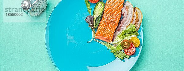 Intermittierendes Fasten niedrige Kohlenhydrate hohe Fette Diät-Konzept flach legen  gesunde Lebensmittel Lachs Fisch  Speck Fleisch  Gemüse und Salat auf blauem Teller und Wecker auf blauem Hintergrund Ansicht von oben