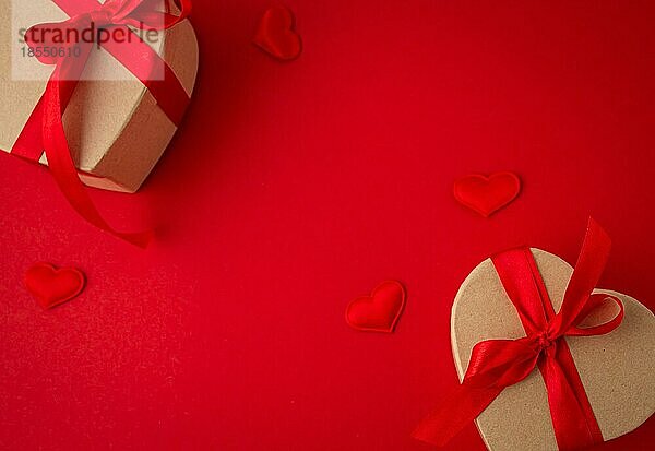 Zwei verpackte Geschenk-Boxen in Herzform mit roter Schleife Band auf rotem Hintergrund und kleine gepolsterte Herzen Draufsicht flach legen  Geschenke für Saint Valentine Tag  Liebe und Beziehung Konzept  Platz für Text