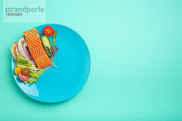 Intermittierendes Fasten niedrige Kohlenhydrate hohe Fette Diät-Konzept flach legen  gesunde Lebensmittel Lachs Fisch  Speck Fleisch  Gemüse und Salat auf blauem Teller auf blauem Hintergrund Draufsicht  Platz für Text