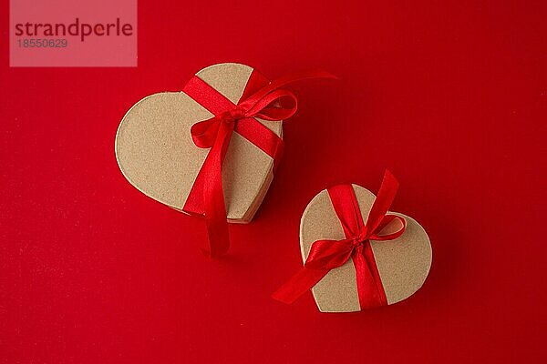 Zwei verpackte Geschenk-Boxen in Herzform mit roter Schleife Band auf rotem Hintergrund Draufsicht flach legen  Geschenke für die Feier Saint Valentine Tag  Liebe und Beziehung Konzept