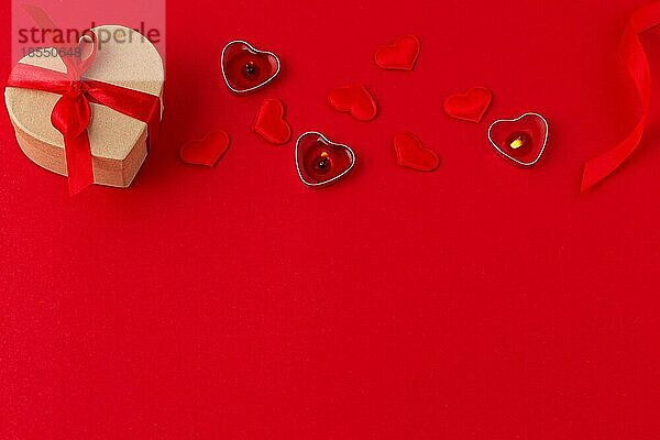 Saint Valentine flach legen Draufsicht Komposition: herzförmige Geschenk-Box mit rotem Band  leuchtende Kerzen  kleine gepolsterte Herzen auf rotem Papier Hintergrund  Liebe und romantische Geschenk  Platz für Text