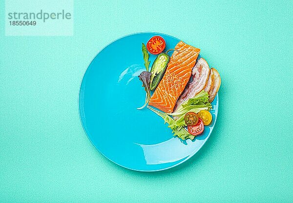 Intermittierendes Fasten niedrige Kohlenhydrate hohe Fette Diät-Konzept flach legen  gesunde Lebensmittel Lachs Fisch  Speck Fleisch  Gemüse und Salat auf blauem Teller und blauem Hintergrund von oben gesehen
