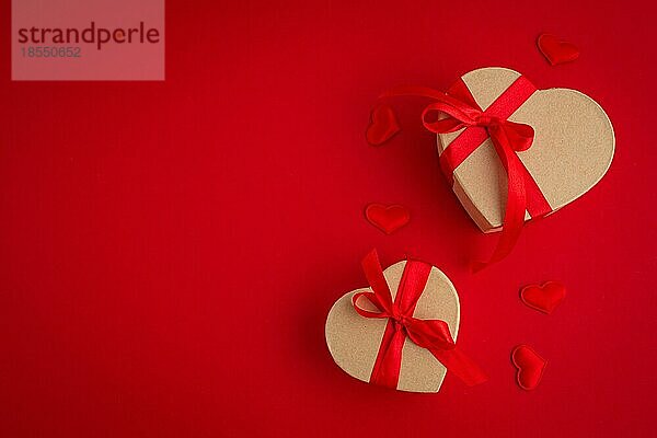 Zwei verpackte Geschenk-Boxen in Herzform mit roter Schleife Band auf rotem Hintergrund und kleine gepolsterte Herzen Draufsicht flach legen  Geschenke für Saint Valentine Tag  Liebe und Beziehung Konzept