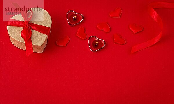 Saint Valentine flach legen Draufsicht Komposition: herzförmige Geschenk-Box mit rotem Band  leuchtende Kerzen  kleine gepolsterte Herzen auf rotem Papier Hintergrund  Liebe und romantische Geschenk  Platz für Text