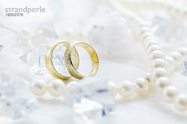 Zwei goldene Ringe mit Perlenkette und auf weißem Hintergrund als Symbol der Liebe und Ehe