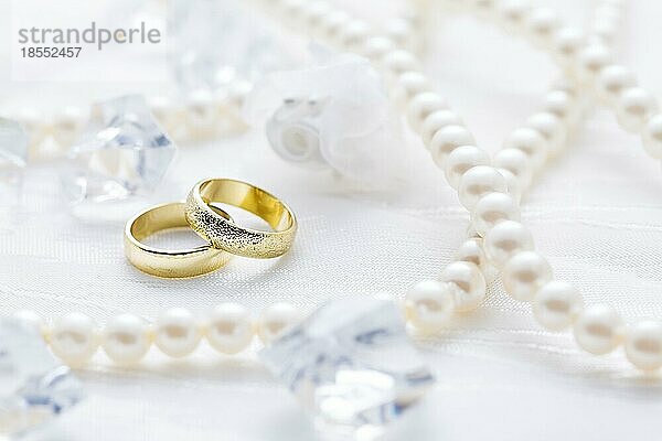 Zwei goldene Ringe mit Perlenkette und auf weißem Hintergrund als Symbol der Liebe und Ehe