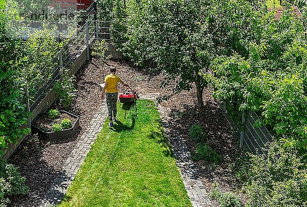 Junge schneidet das Gras mit elektrischem Rasenmäher. Gartenarbeit Konzept. Ansicht von oben