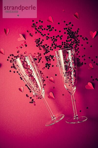 Zwei Champagnergläser mit einem Spritzer rotem herzförmigen Konfetti auf rotem Hintergrund. Overhead Ansicht  Kopie Raum. Valentinstag Konzept