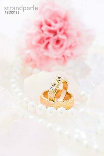 Goldene Eheringe mit Perlenkette mit rosa Blume im Hintergrund  Weichzeichner