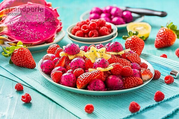 Frischer Drachenfruchtsalat mit Erdbeeren  Himbeeren und Sternfrucht (Karambole) auf cyanfarbenem Hintergrund
