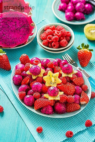 Frischer Drachenfruchtsalat mit Erdbeeren  Himbeeren und Sternfrucht (Karambole) auf cyanfarbenem Hintergrund