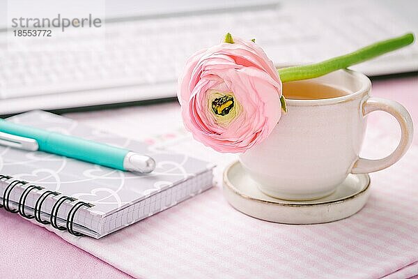 Schreibtisch im Heimbüro mit Tasse Tee  Blume  Tastaturen und Schreibutensilien