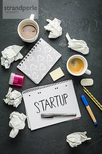 Startup Konzept Notizblock  Kaffee  verworfene Ideen und Schreibgeräte auf schwarzem Schreibtisch
