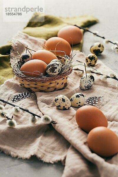 Eier und Wachteleier für Ostern und blühende Trauerweidenzweige auf hölzernem Hintergrund