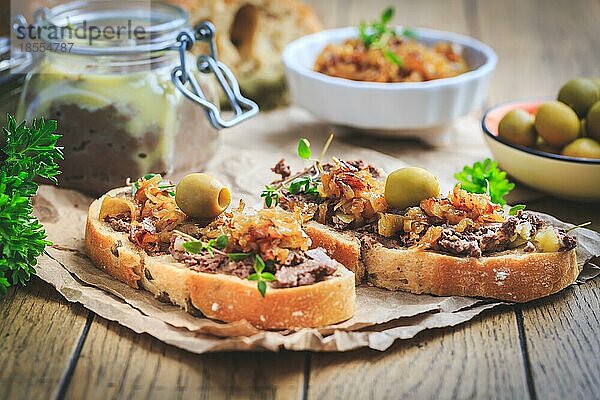 Frische hausgemachte Hühnerleberpastete auf Ciabatta Brot mit gerösteten Zwiebeln und Oliven auf Holztisch