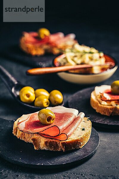 Geröstetes Brot oder offenes Sandwich mit Knoblauchbutteraufstrich und Serano Schinken und Oliven auf dunklem Hintergrund