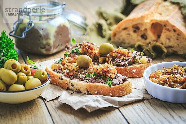 Frische hausgemachte Hühnerleberpastete auf Ciabatta Brot mit gerösteten Zwiebeln und Oliven auf Holztisch