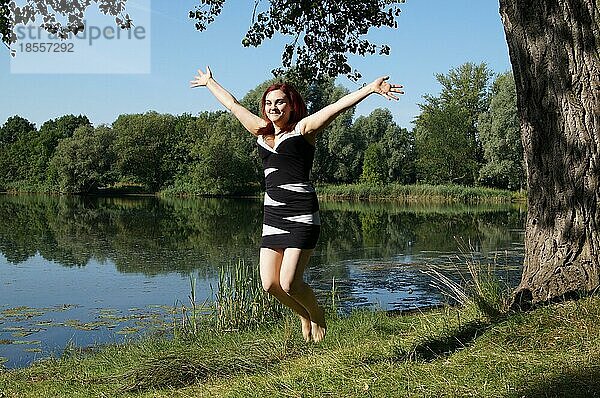 Junge Frau springt vor Freude an einem Seeufer