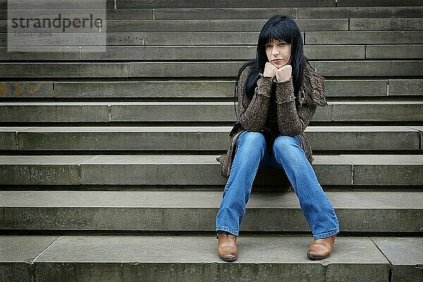 Einsame Frau  die draußen auf den Stufen sitzt