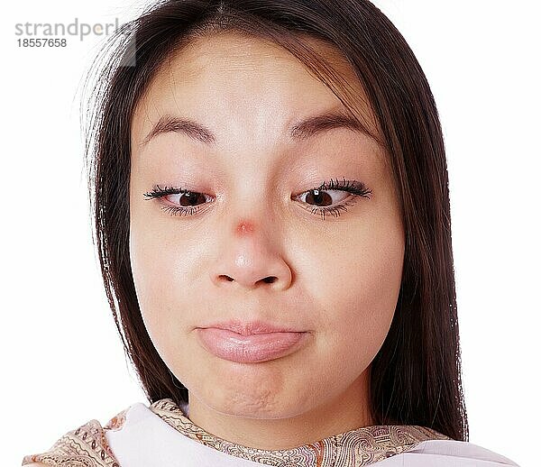 Junge asiatische Frau schielt auf einen roten Pickel auf ihrer Nase