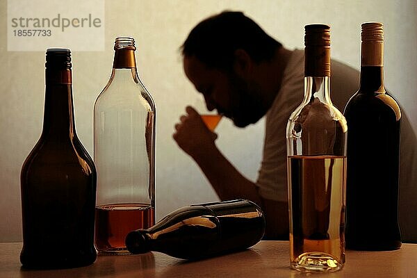 Silhouette einer anonymen alkoholabhängigen Person  die hinter Flaschen Alkohol trinkt