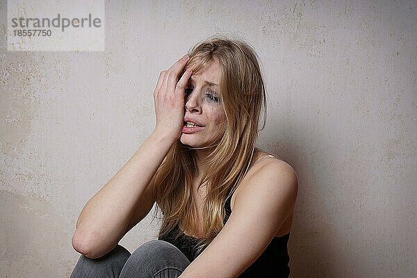 Traurige junge Frau mit tränenverschmiertem Gesicht und verschmiertem Make-up vom Weinen