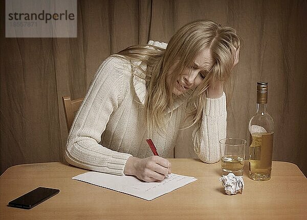 Liebeskranke junge Frau schreibt Brief mit Whiskeyflasche auf dem Tisch