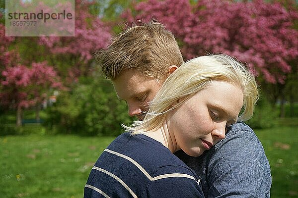 Junges Paar in Umarmung mit ihrem Kopf auf seiner Schulter in einem Park