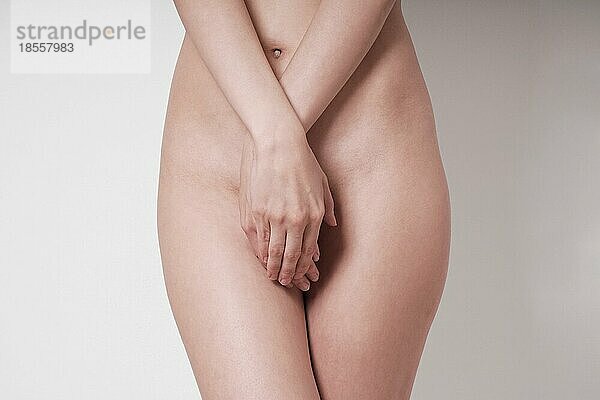Mittelteil einer unkenntlichen nackten Frau  die ihre Geschlechtsteile oder ihren Genitalbereich mit den Händen bedeckt