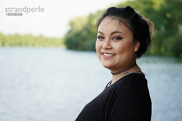 Glückliche junge asiatische Frau am Seeufer stehend
