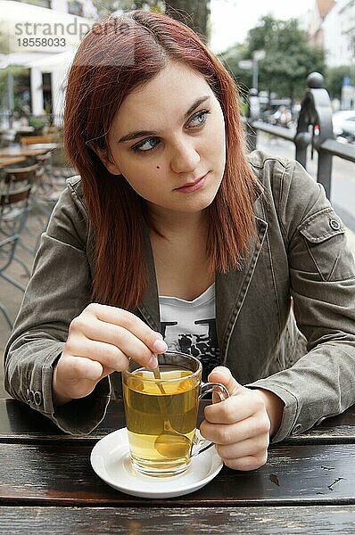 Junge Frau trinkt Tee in einem Straßencafé