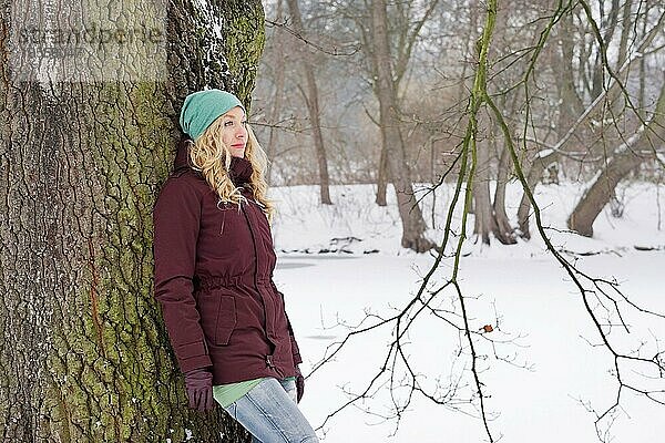 Nachdenkliche Frau lehnt an einer Birke in einer verschneiten Winterlandschaft