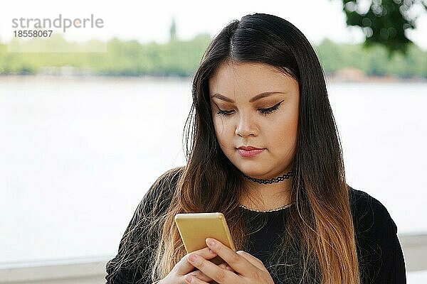 Junge asiatische Frau  die eine Textnachricht auf ihrem Smartphone liest