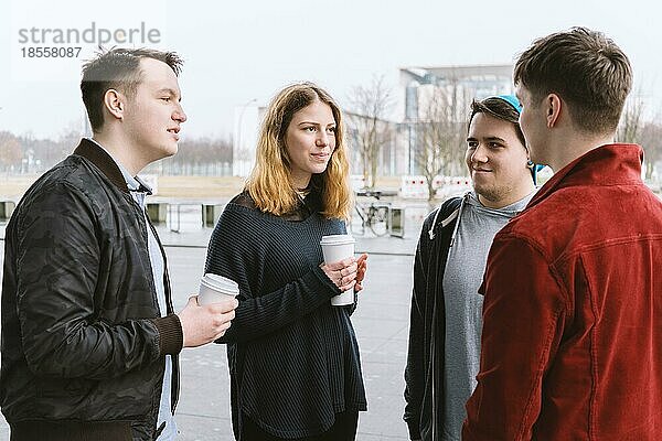 Eine Gruppe von Freunden im Teenageralter  die sich unterhalten  während sie zusammen auf der Straße stehen und Kaffeetassen in der Hand halten
